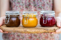 closeup-view-of-woman-holding-wooden-plate-with-plum-apricot-raspberry-jam-glass-jars